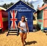 Larissa nas Brighton Beach Bathing Boxes em Melbourne, em frente à casinha com a bandeira australiana — Austrália