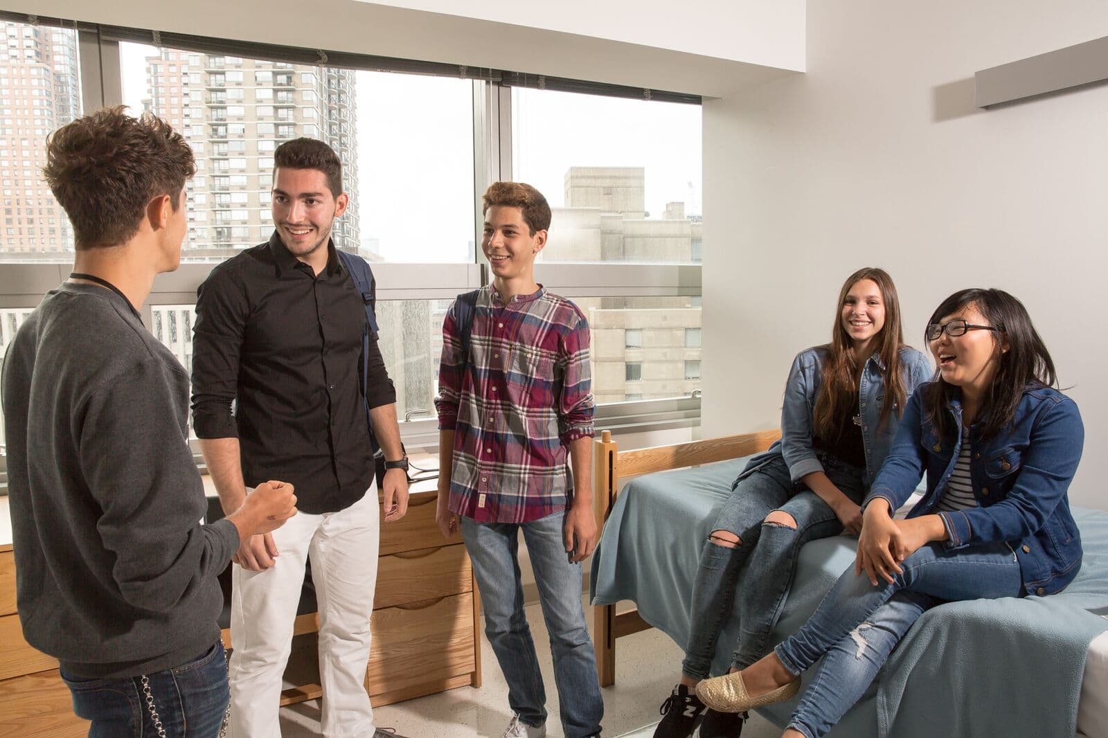 Alunos conversando num quarto da residência em Manhattan, com prédios na janela