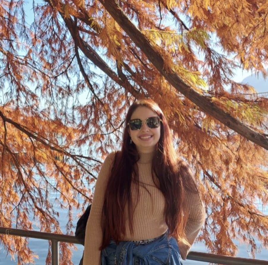 Bianca sorrindo embaixo de uma árvore de folhas alaranjadas