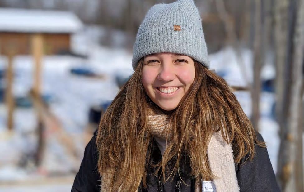 Aluna sorrindo de gorro na neve